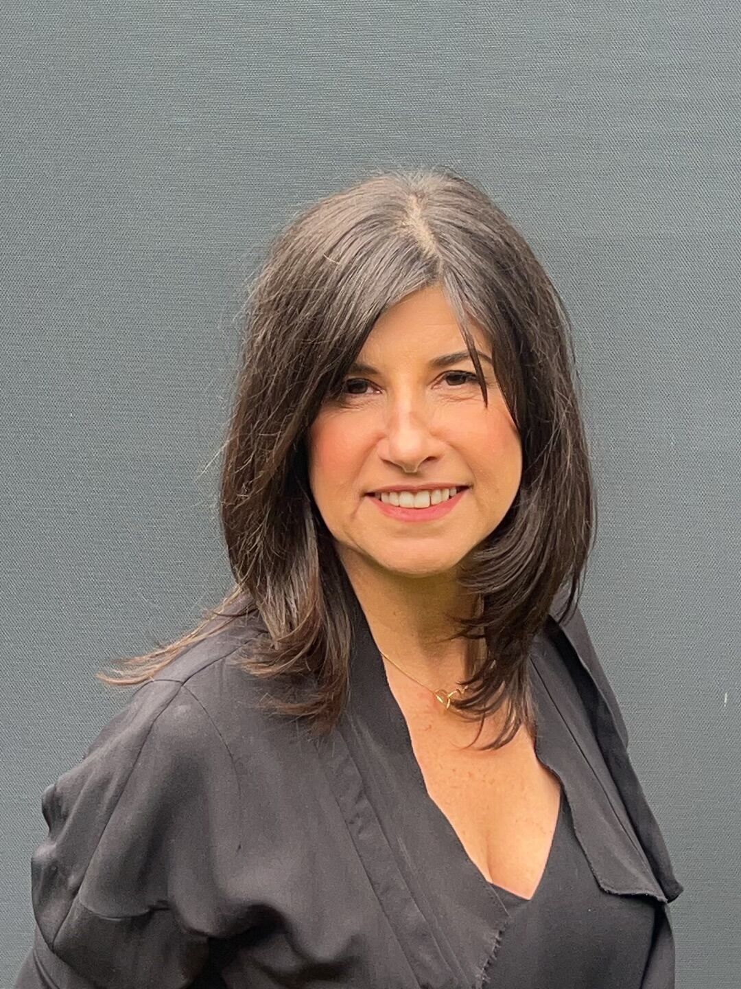 Portrait of Alida Milani, founder of The Artisanal Collective, in a dark top against a grey wall.